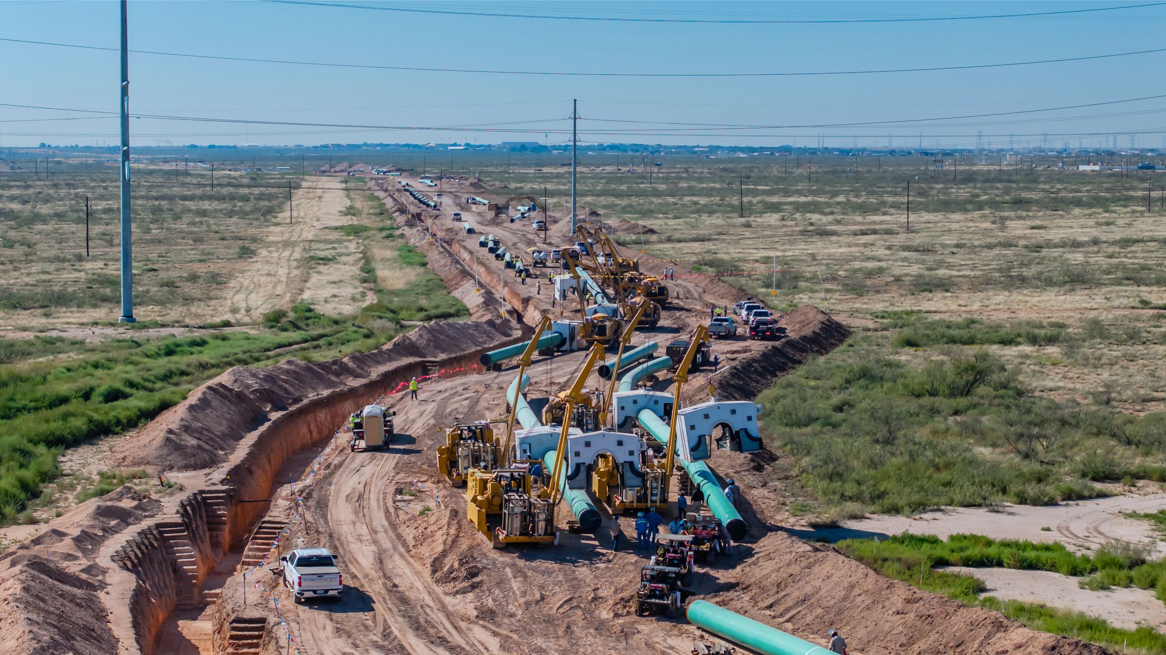 Aerial view of a pipeline construction spread — coated pipe string, sidebooms and welding habitats along an open right-of-way