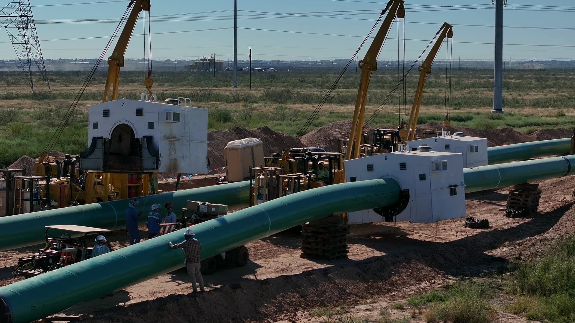 Aerial view of a pipeline construction spread — large-diameter coated pipe string, sidebooms and welding habitats